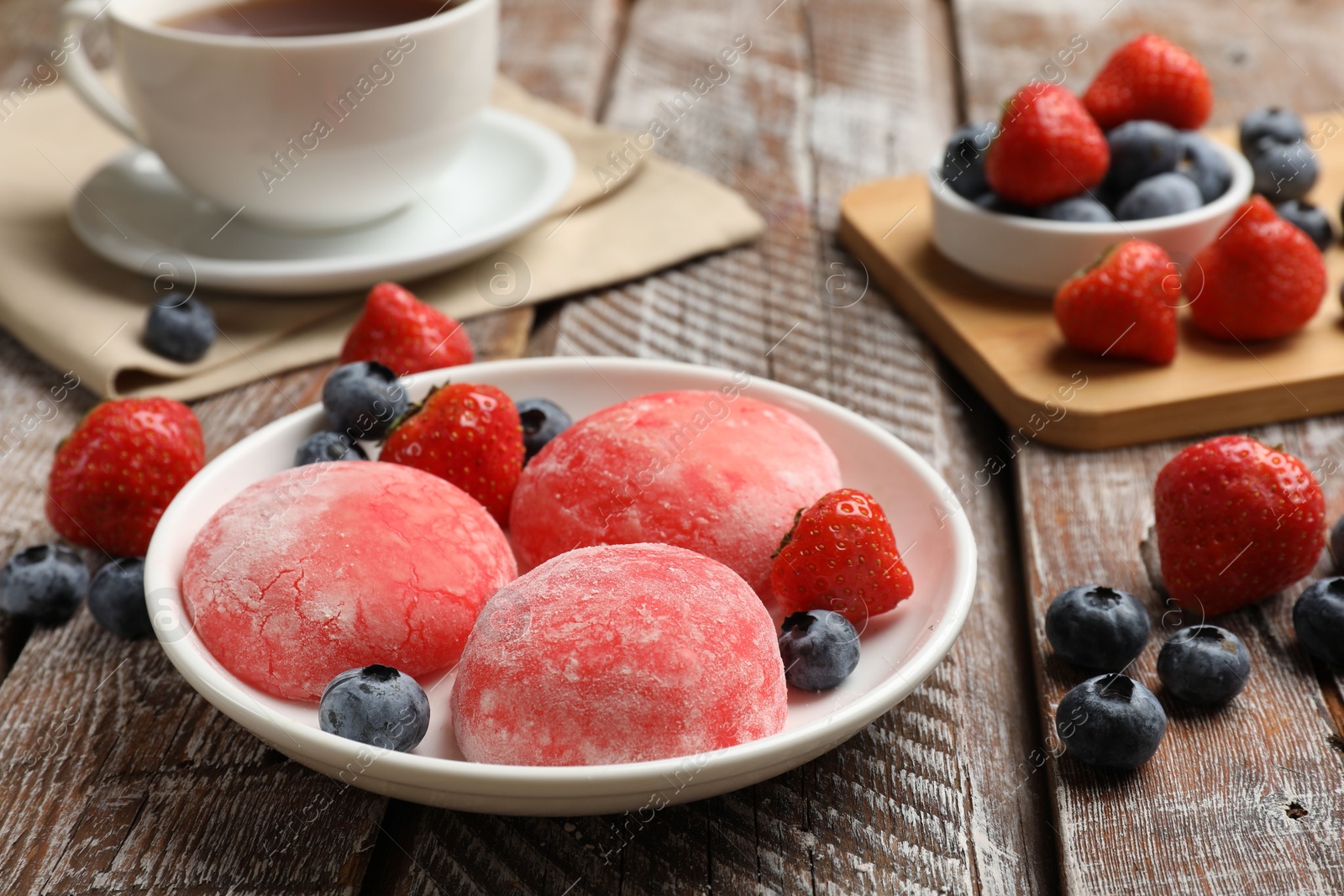 Photo of Delicious mochi, strawberries, blueberries and tea on wooden table, closeup