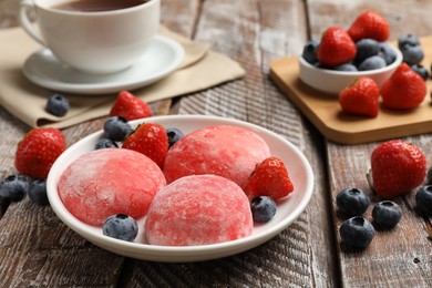 Photo of Delicious mochi, strawberries, blueberries and tea on wooden table, closeup