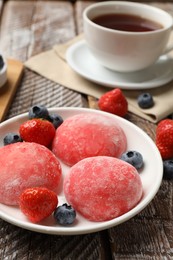 Photo of Delicious mochi, strawberries, blueberries and tea on wooden table, closeup