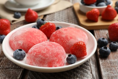 Photo of Delicious mochi, strawberries and blueberries on wooden table, closeup