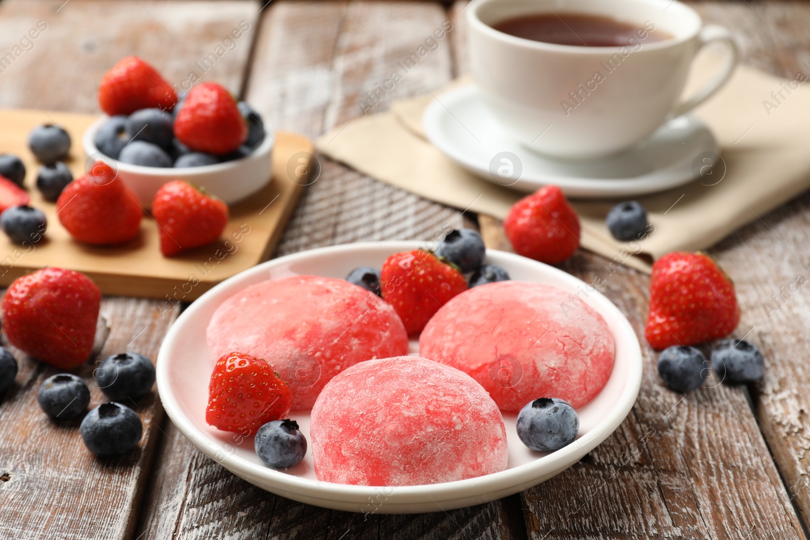 Photo of Delicious mochi, strawberries and blueberries on wooden table, closeup