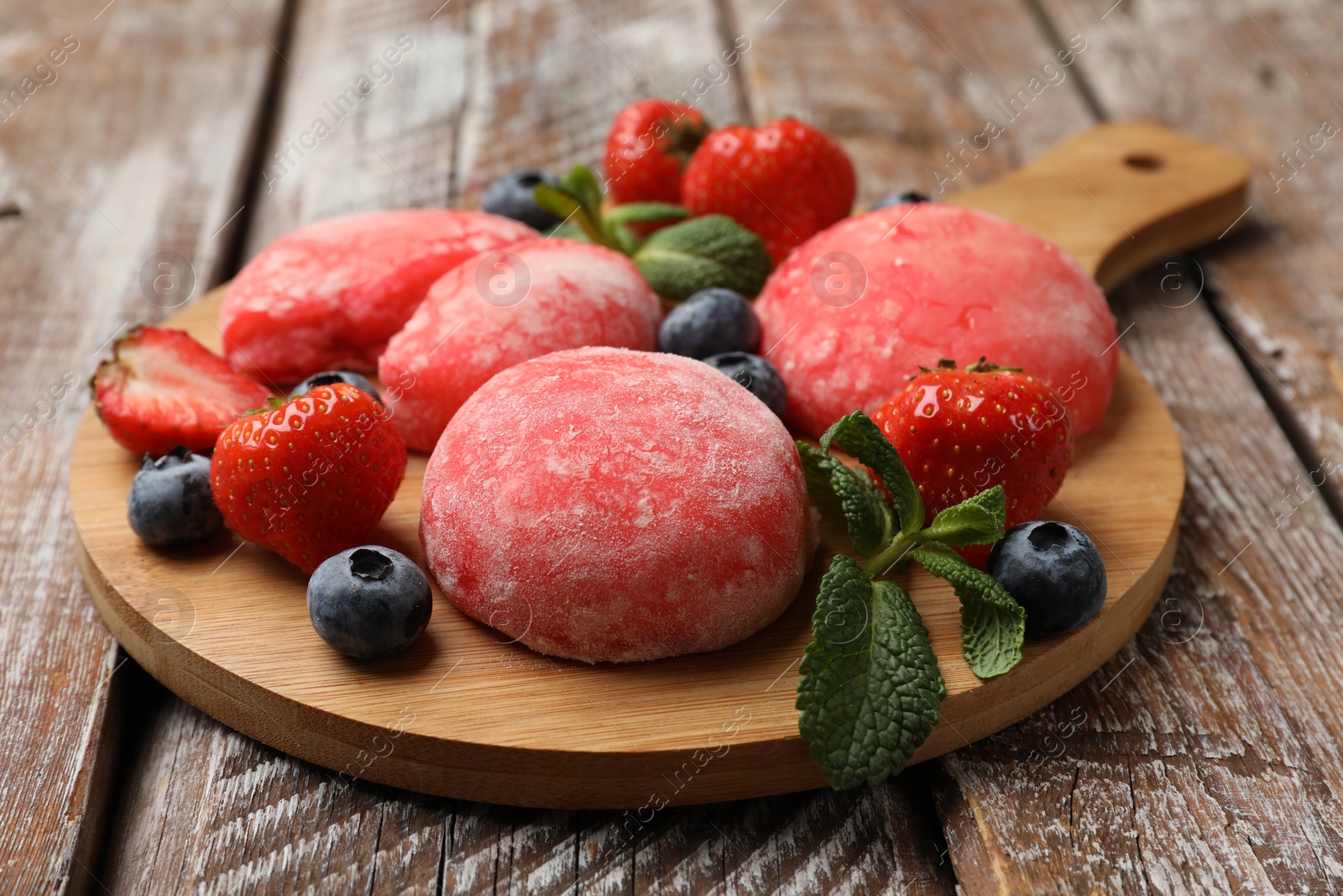 Photo of Delicious mochi, strawberries, blueberries and mint on wooden table, closeup