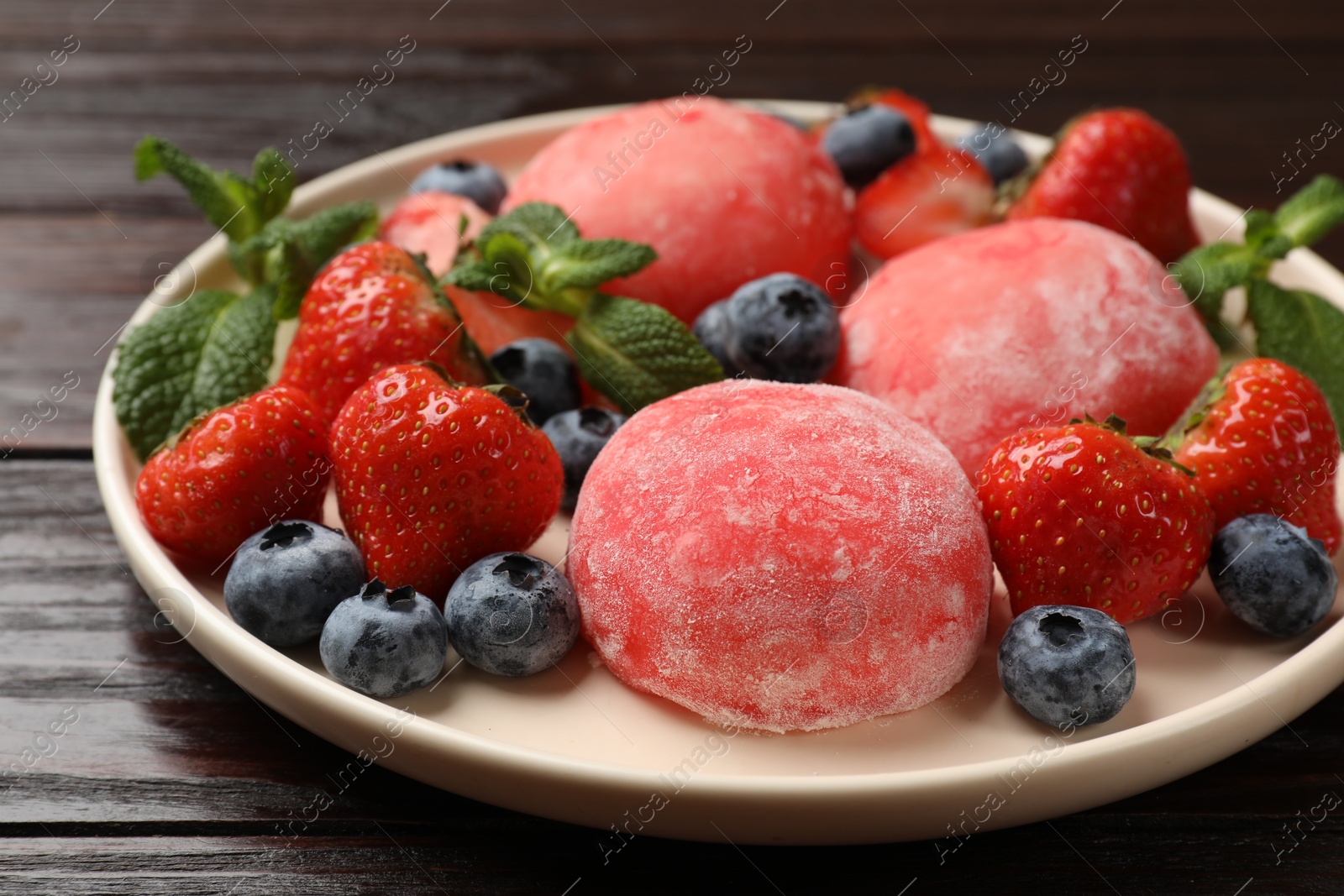 Photo of Delicious mochi, strawberries, blueberries and mint on wooden table, closeup