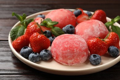 Photo of Delicious mochi, strawberries, blueberries and mint on wooden table, closeup