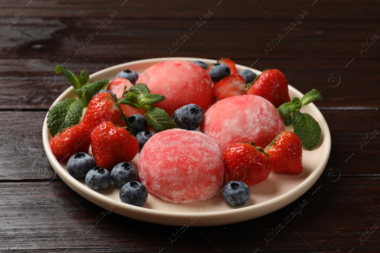 Photo of Delicious mochi, strawberries, blueberries and mint on wooden table, closeup