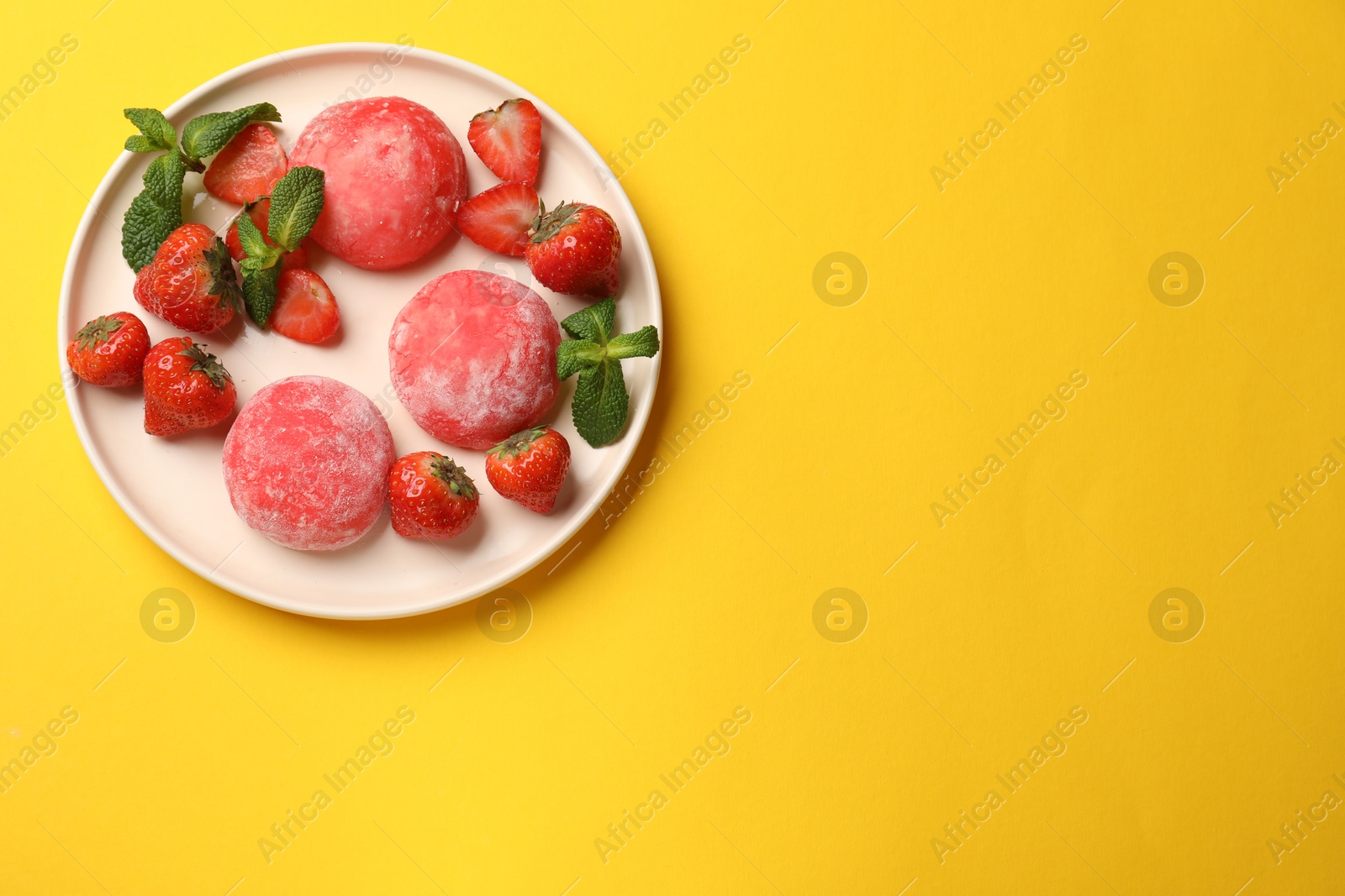 Photo of Delicious mochi, strawberries and mint on yellow table, top view. Space for text