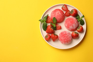 Photo of Delicious mochi, strawberries and mint on yellow table, top view. Space for text