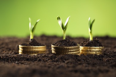 Photo of Stacks of coins with green plants on soil against blurred background, closeup. Money growth concept