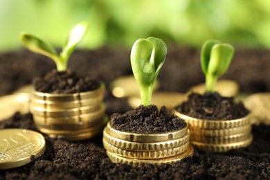 Photo of Stacks of coins with green plants on soil against blurred background, closeup. Money growth concept