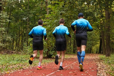 Photo of Group of athletic people running in park, back view