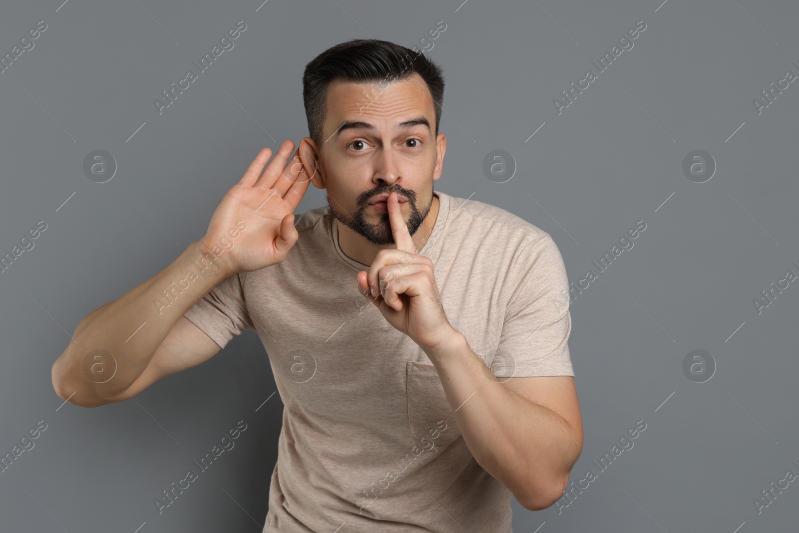 Photo of Man showing hand to ear gesture on grey background