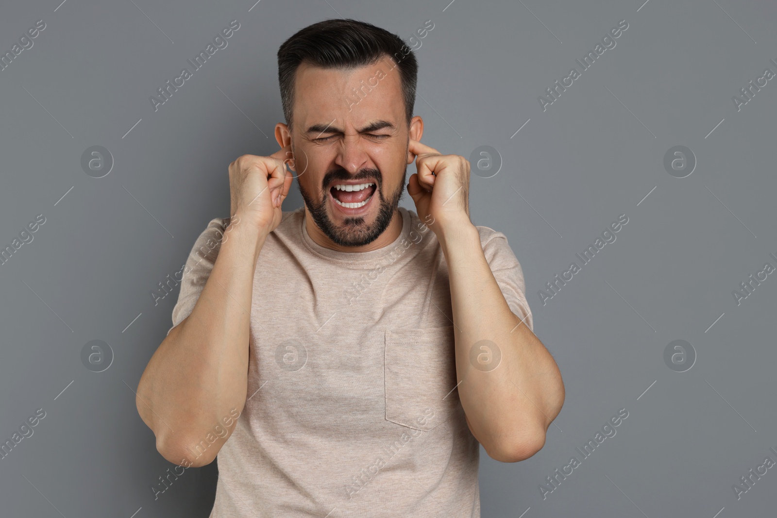 Photo of Man covering his ears with fingers on grey background