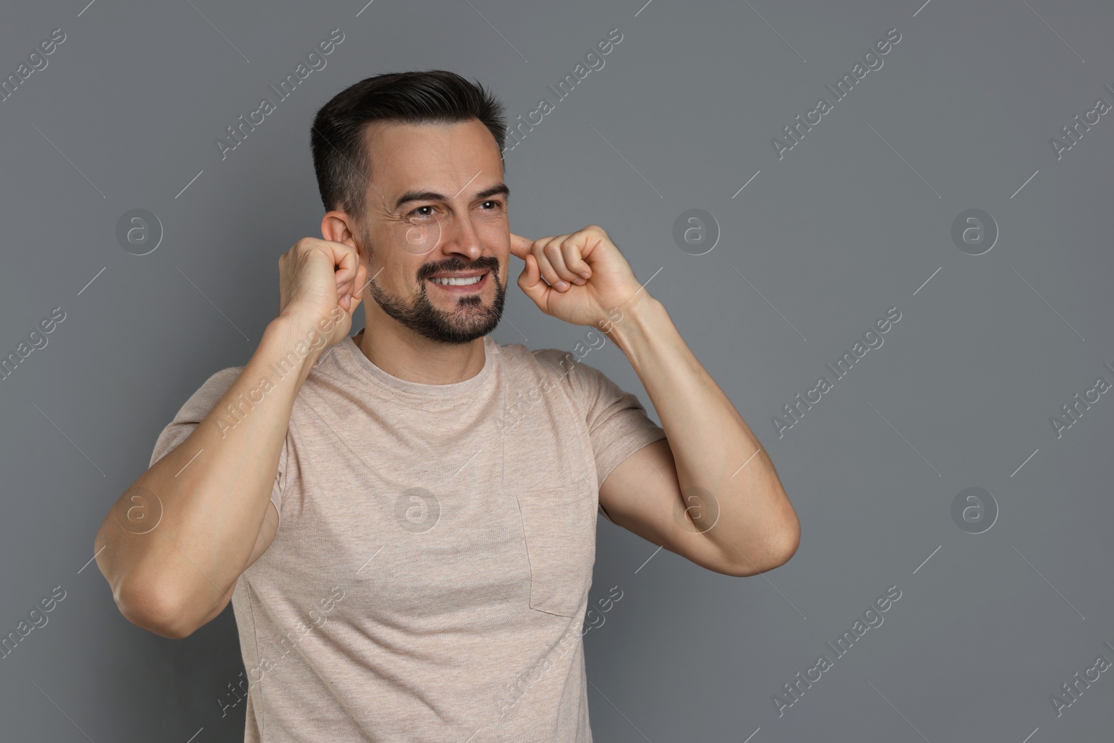 Photo of Man covering his ears with fingers on grey background, space for text