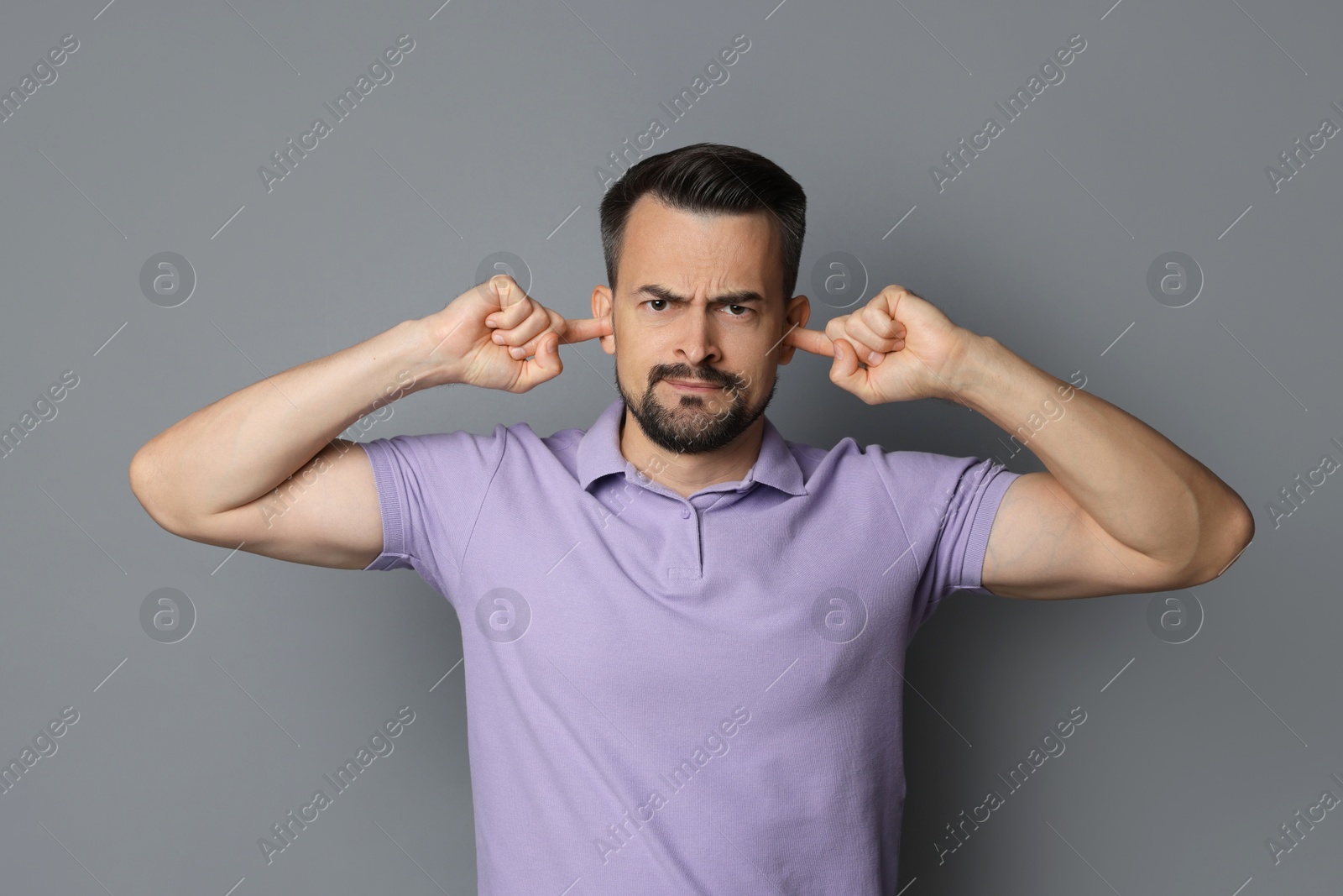 Photo of Man covering his ears with fingers on grey background