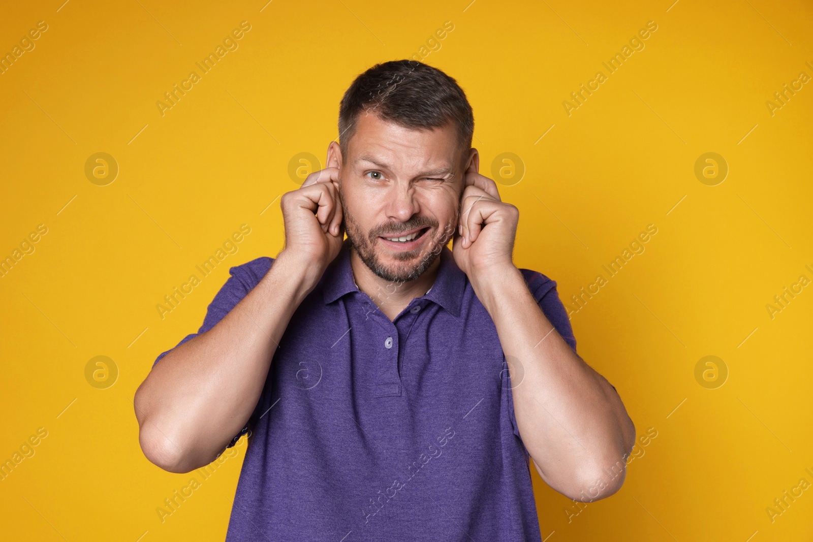 Photo of Man covering his ears with fingers on orange background