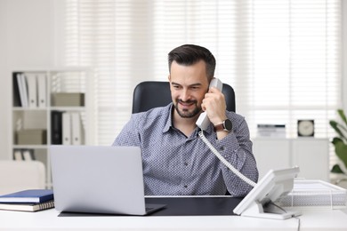 Photo of Happy banker talking on phone at table in office