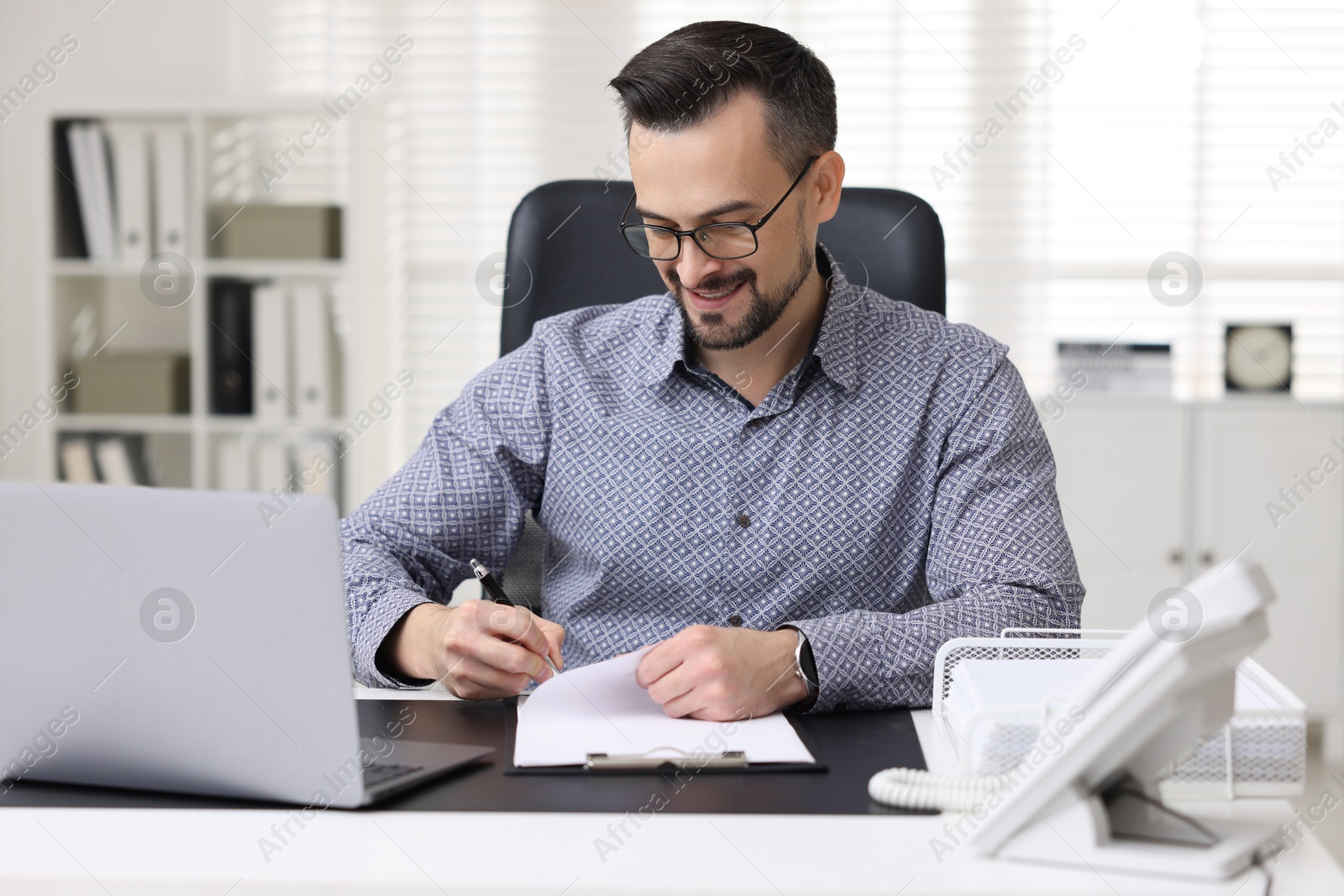 Photo of Handsome banker signing document at table in office