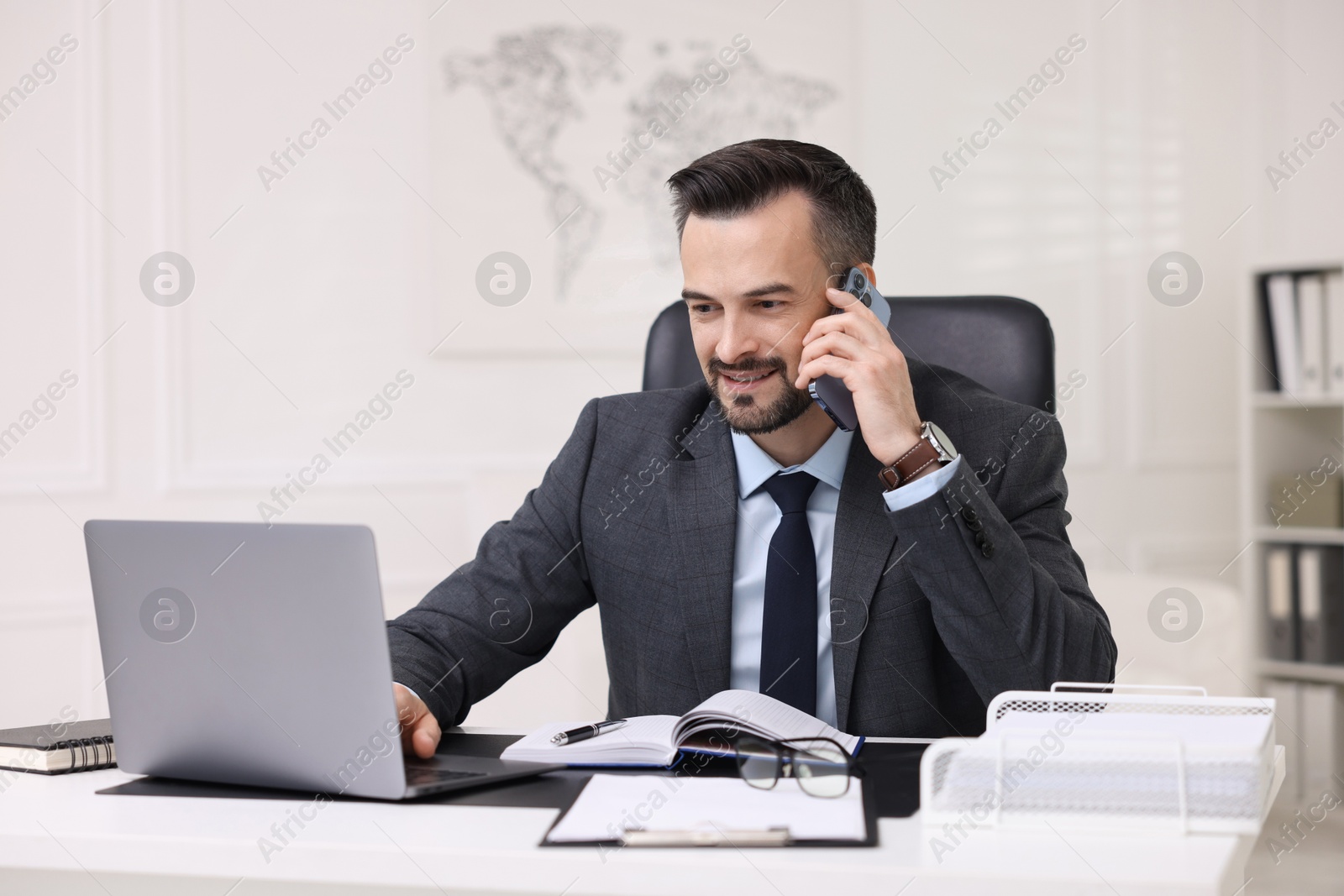 Photo of Happy banker talking on smartphone at table in office