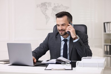 Photo of Happy banker talking on smartphone at table in office