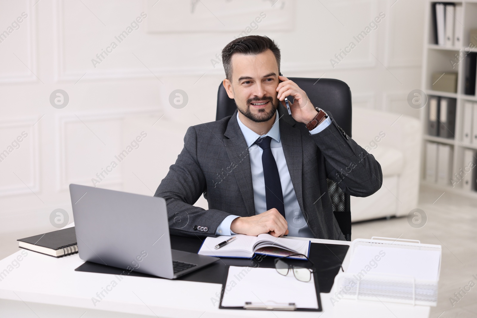 Photo of Happy banker talking on smartphone at table in office