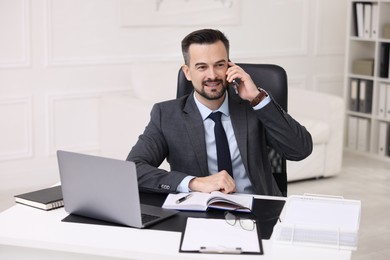 Photo of Happy banker talking on smartphone at table in office