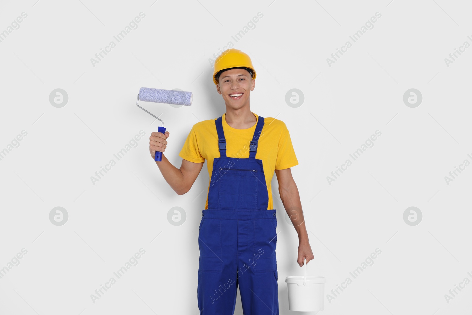 Photo of Portrait of young decorator with paint roller and bucket on white background