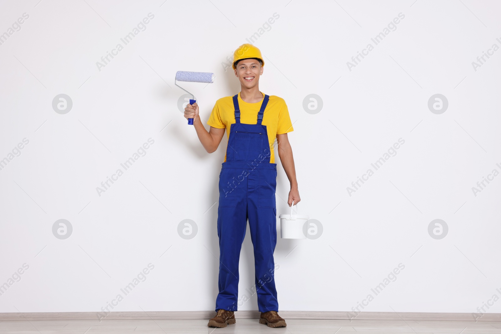 Photo of Young decorator with paint roller and bucket near white wall