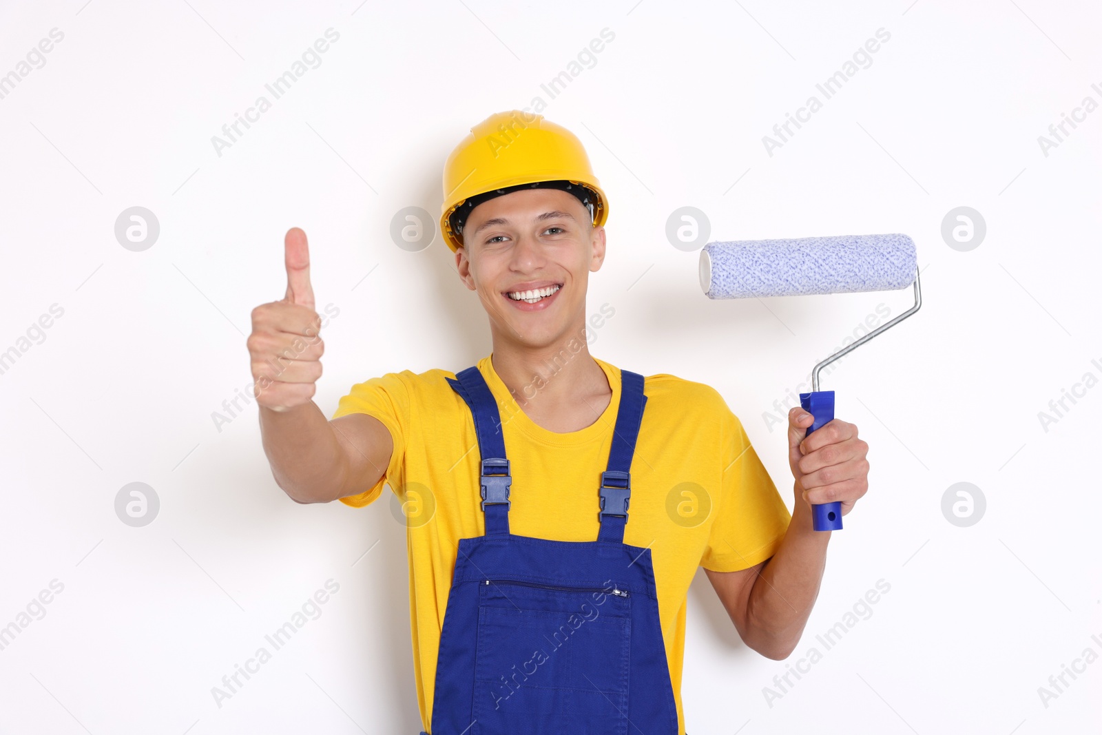 Photo of Portrait of young decorator with paint roller showing thumbs up on white background