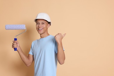 Photo of Portrait of young decorator with paint roller on beige background, space for text