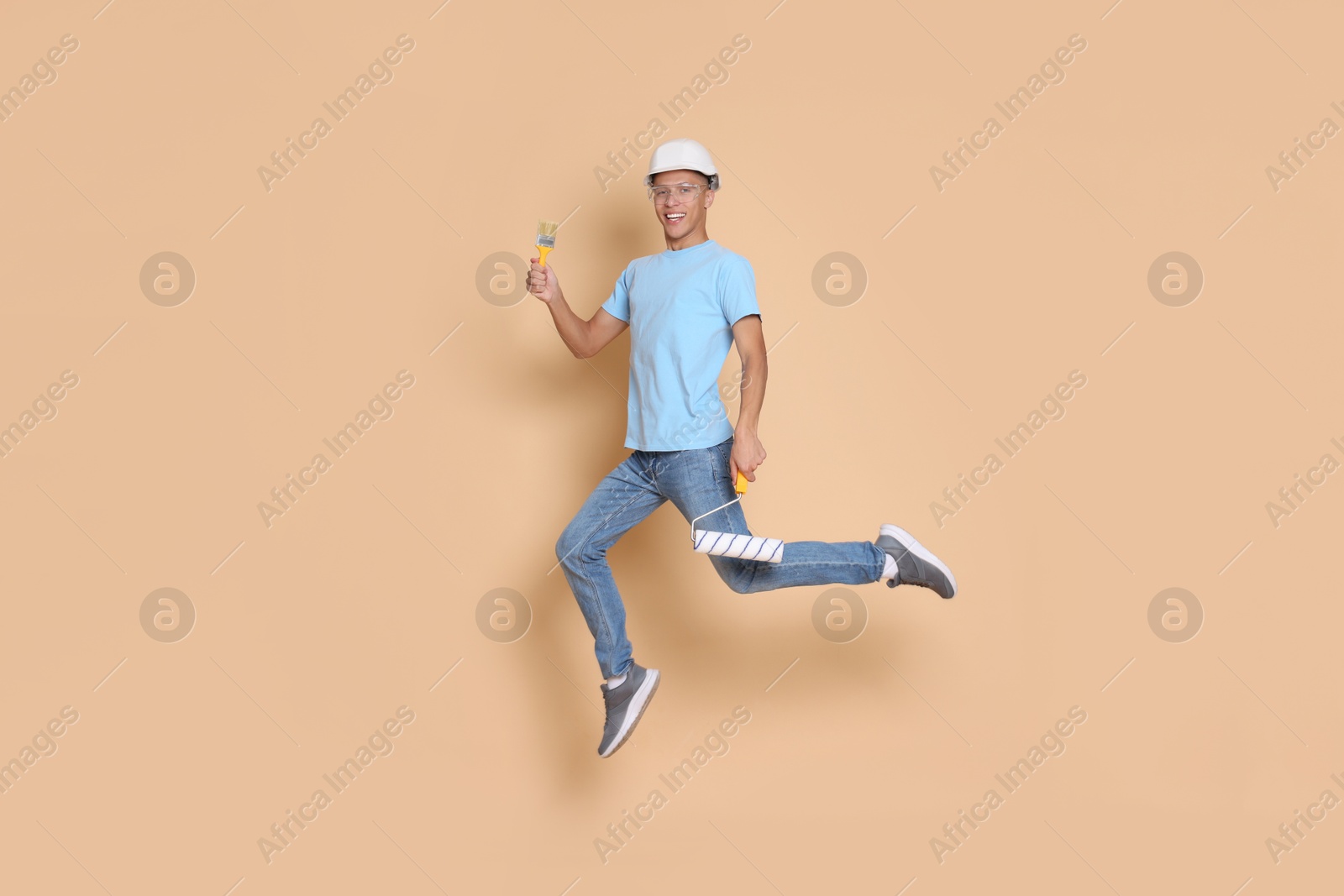 Photo of Young decorator with tools jumping on beige background