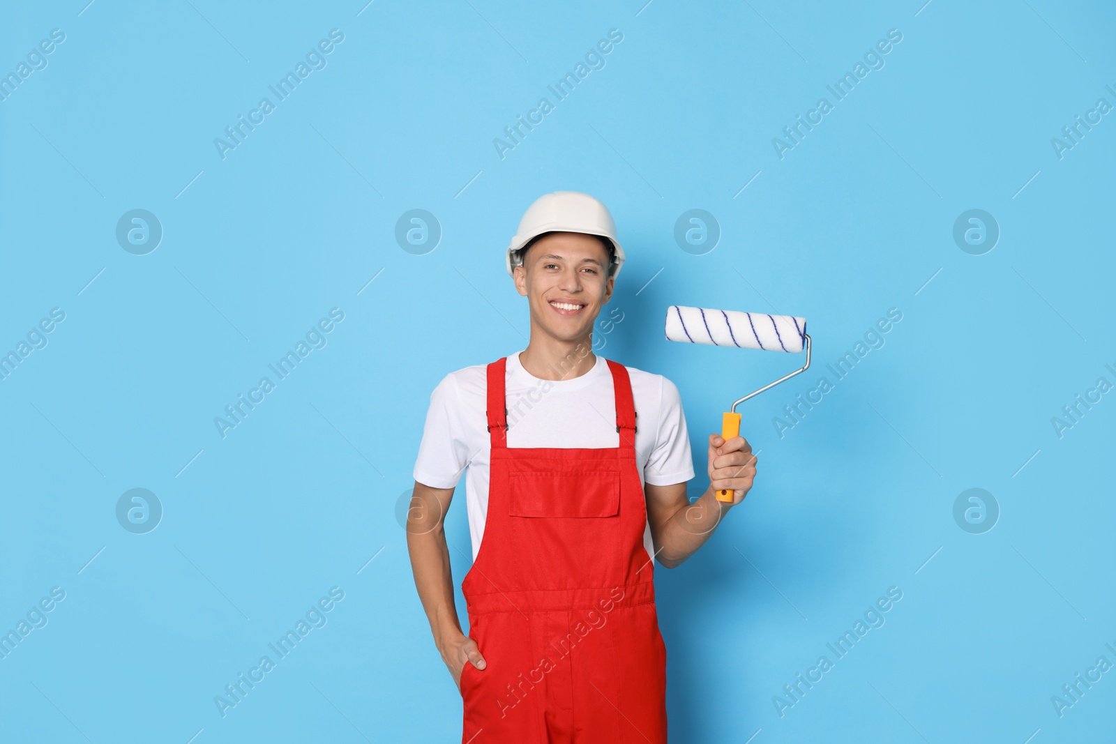 Photo of Portrait of young decorator with paint roller on light blue background