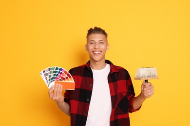 Photo of Portrait of young decorator with color palettes and brush on orange background