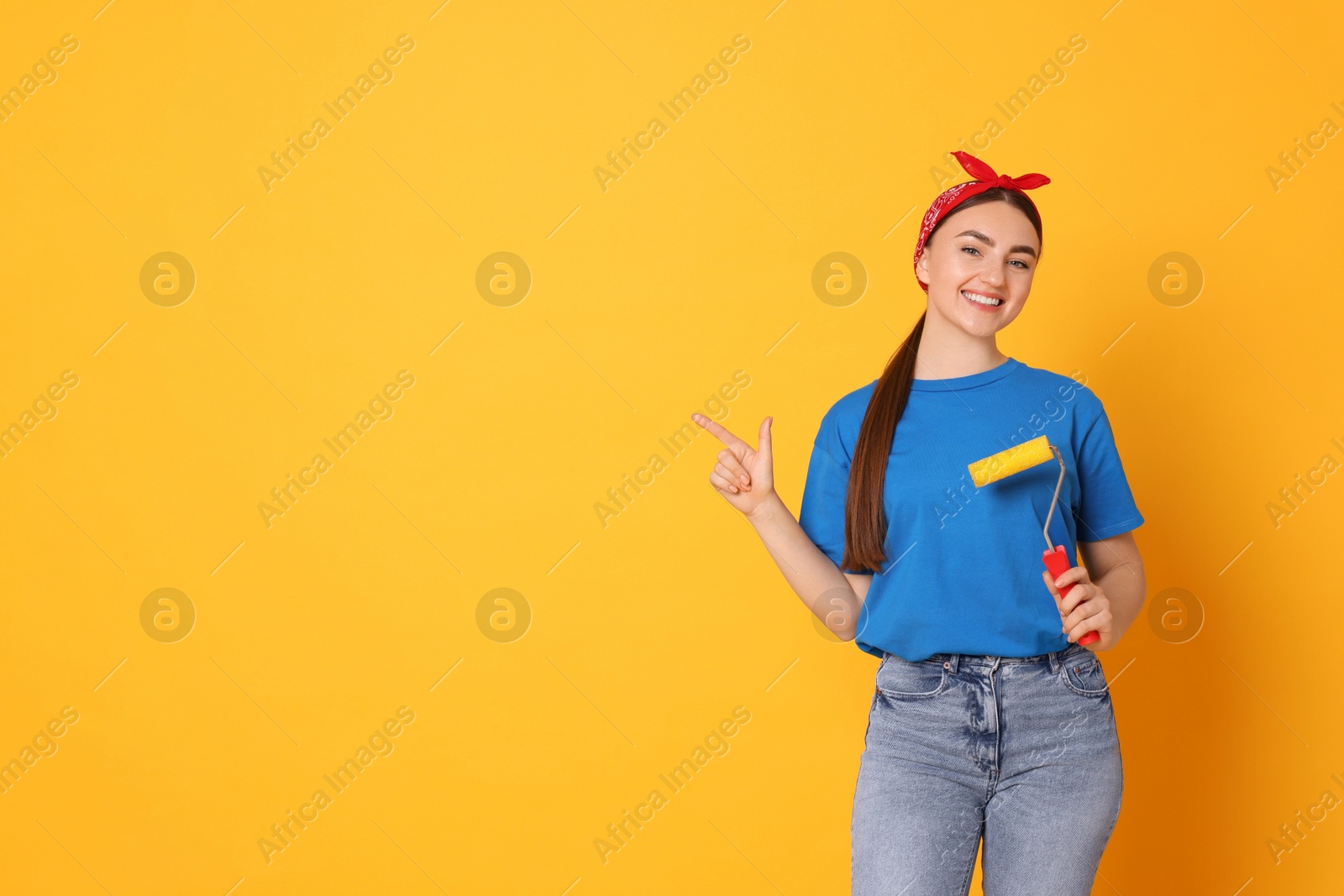 Photo of Portrait of young decorator with paint roller on orange background, space for text