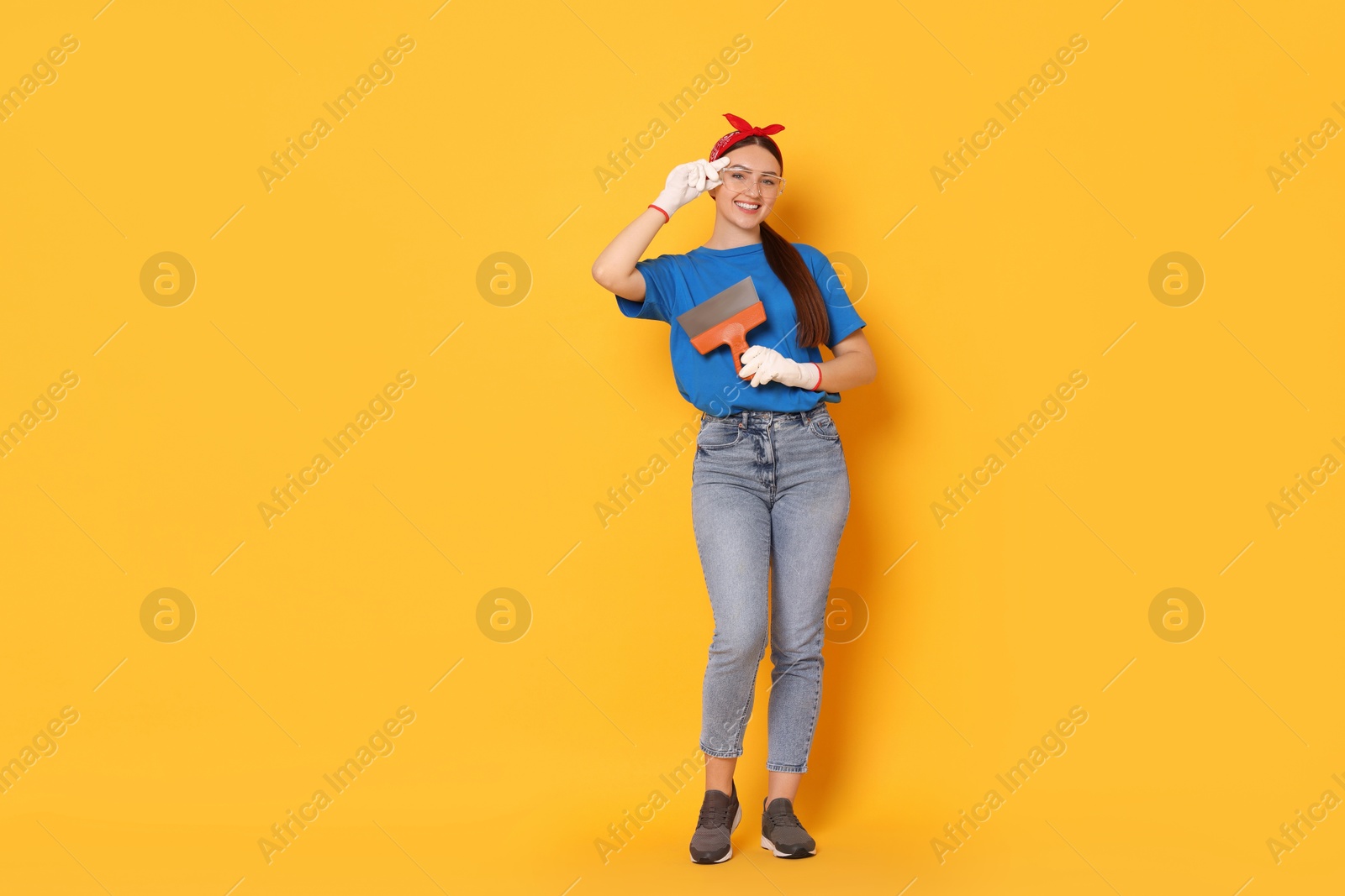 Photo of Young decorator with putty knife on orange background