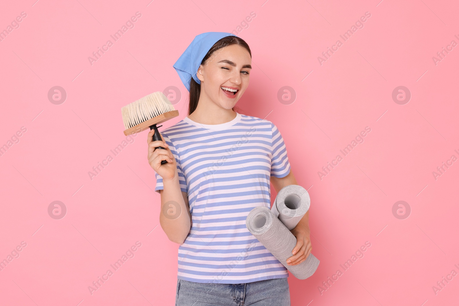 Photo of Young decorator with rolls of wallpaper and brush on pink background