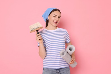 Photo of Young decorator with rolls of wallpaper and brush on pink background