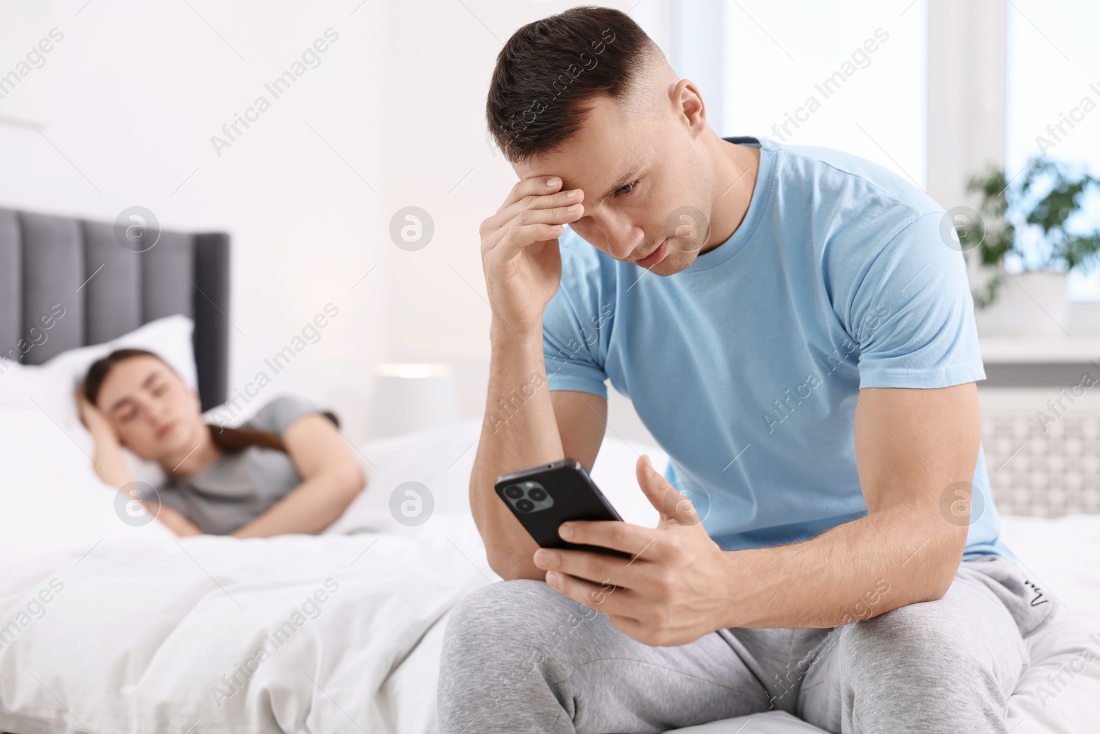 Photo of Upset man checking wife's smartphone while she sleeping in bedroom, selective focus