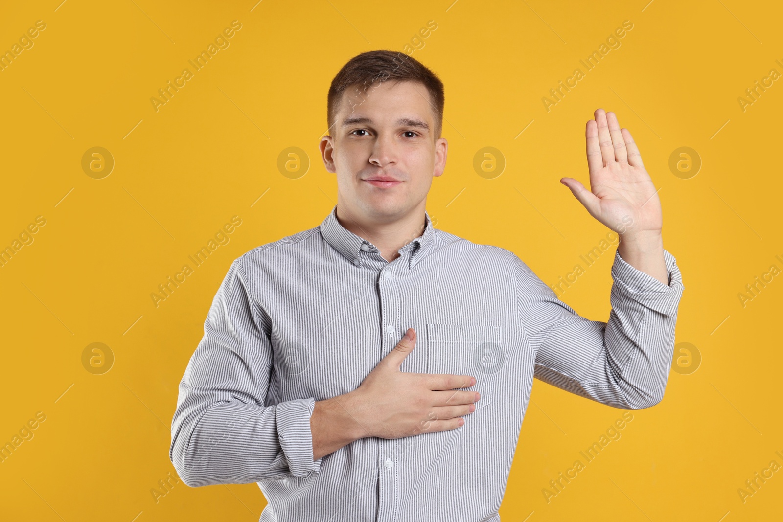 Photo of Man making promise with raised hand on orange background. Oath gesture