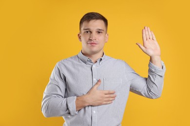 Photo of Man making promise with raised hand on orange background. Oath gesture