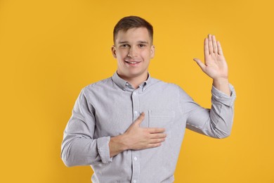 Photo of Man making promise with raised hand on orange background. Oath gesture