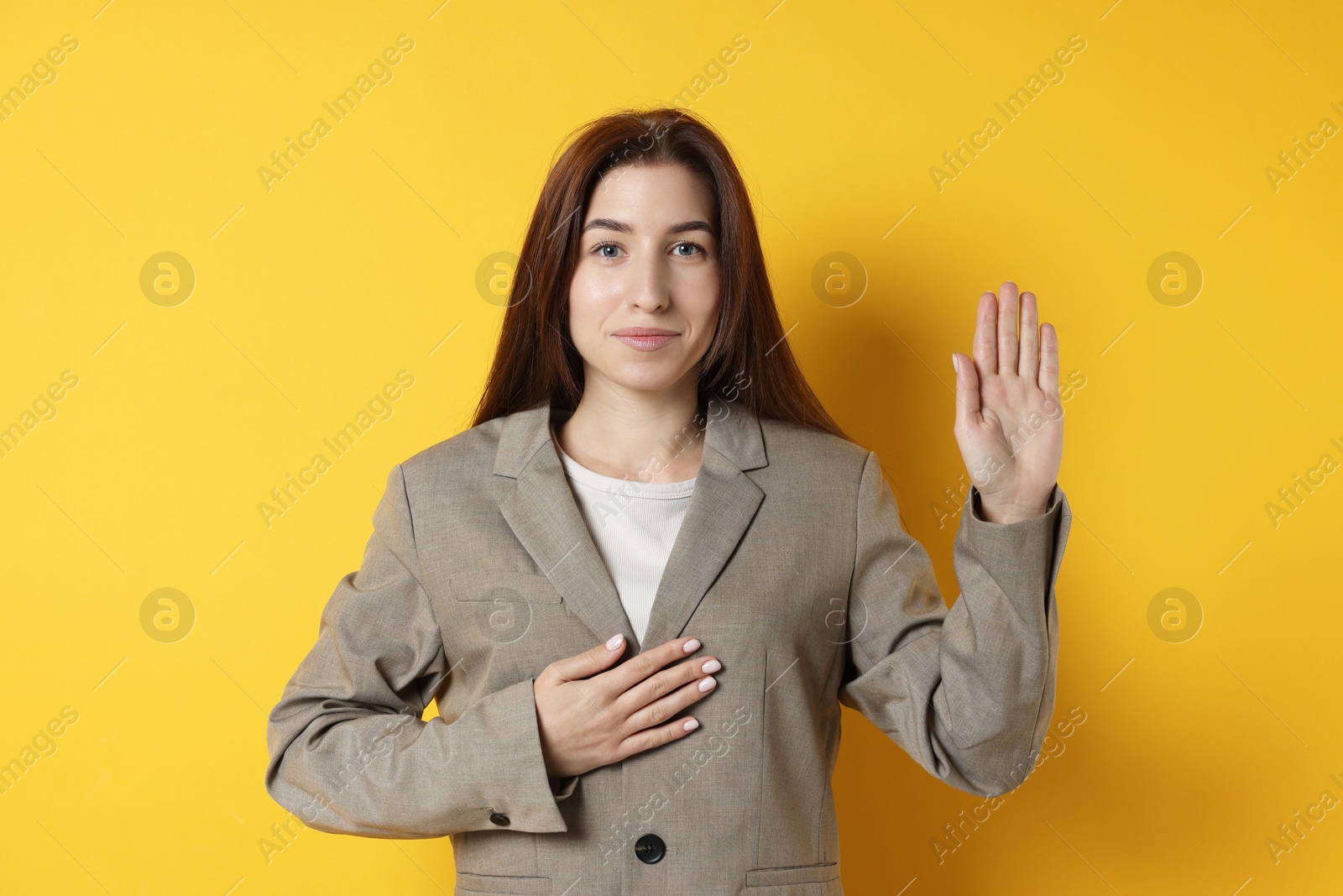 Photo of Woman making promise with raised hand on orange background. Oath gesture