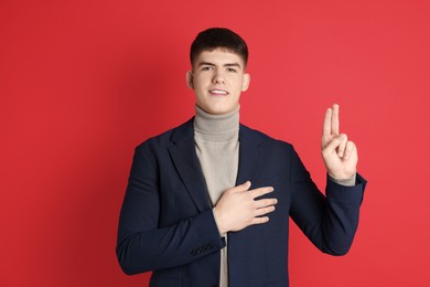 Photo of Man showing oath gesture on red background. Making promise