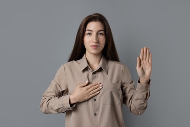 Woman making promise with raised hand on grey background. Oath gesture