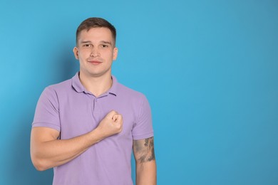 Photo of Man making promise on light blue background, space for text. Oath gesture