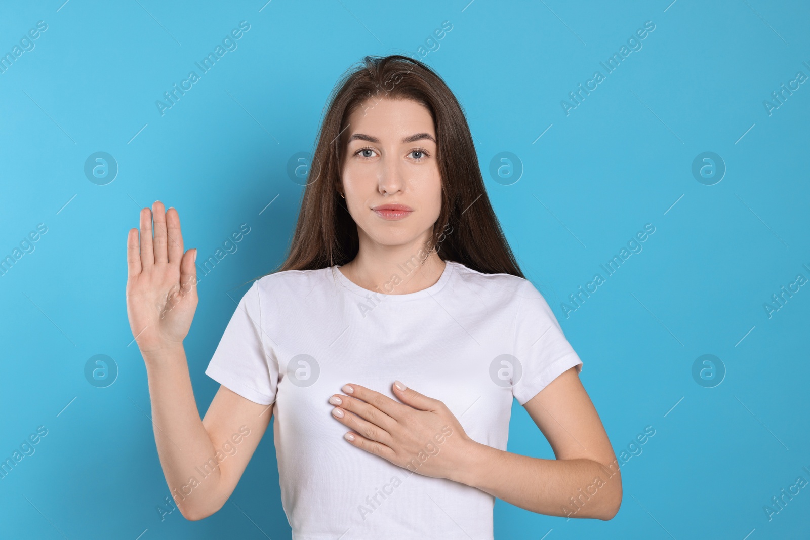 Photo of Woman making promise with raised hand on light blue background. Oath gesture