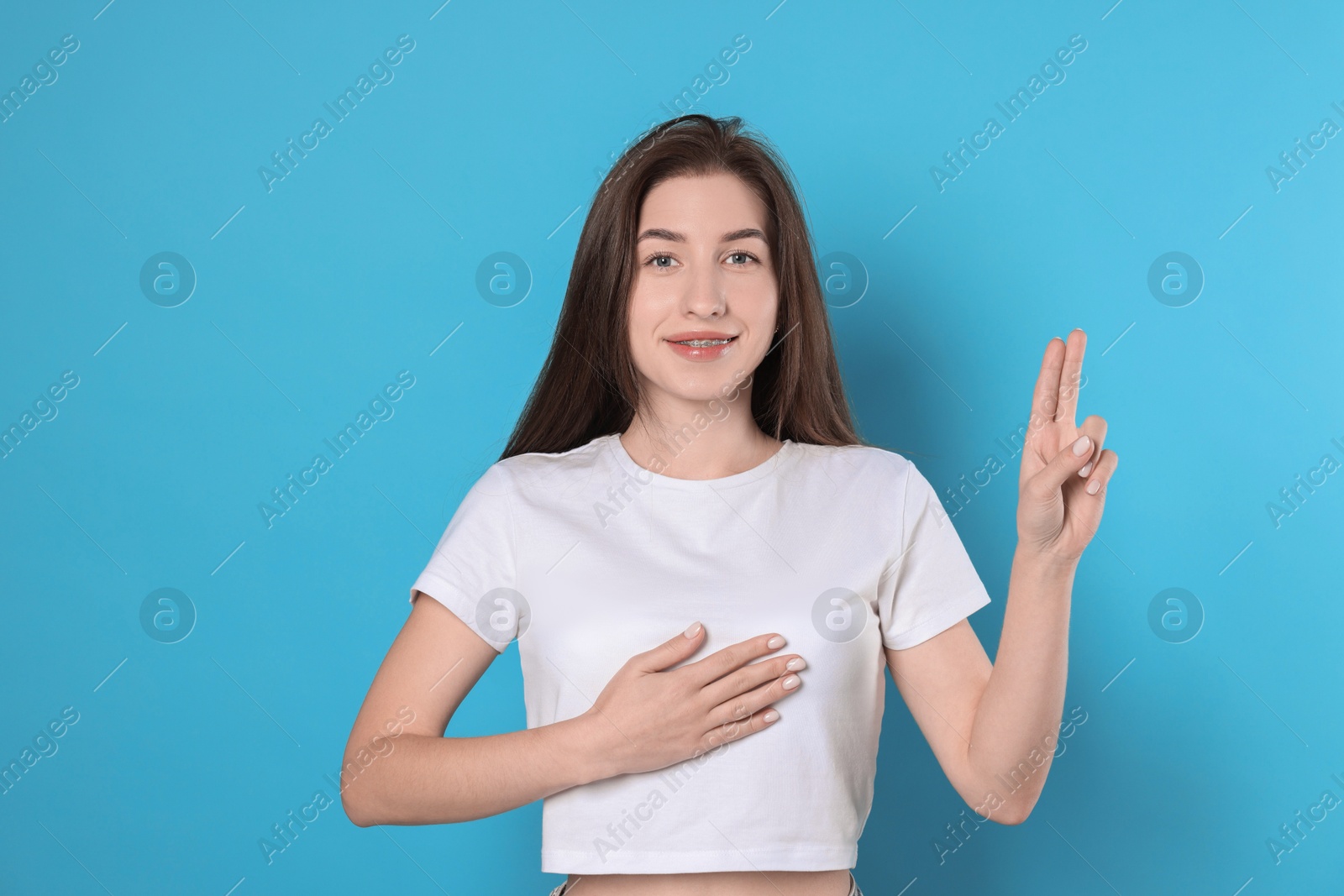 Photo of Woman showing oath gesture on light blue background. Making promise