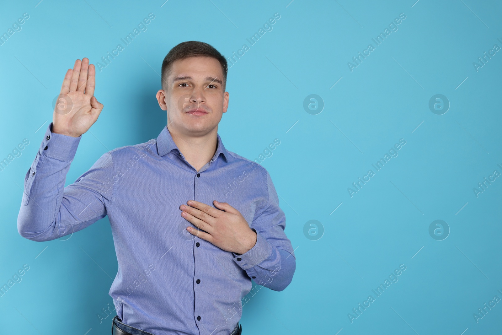 Photo of Man making promise with raised hand on light blue background, space for text. Oath gesture