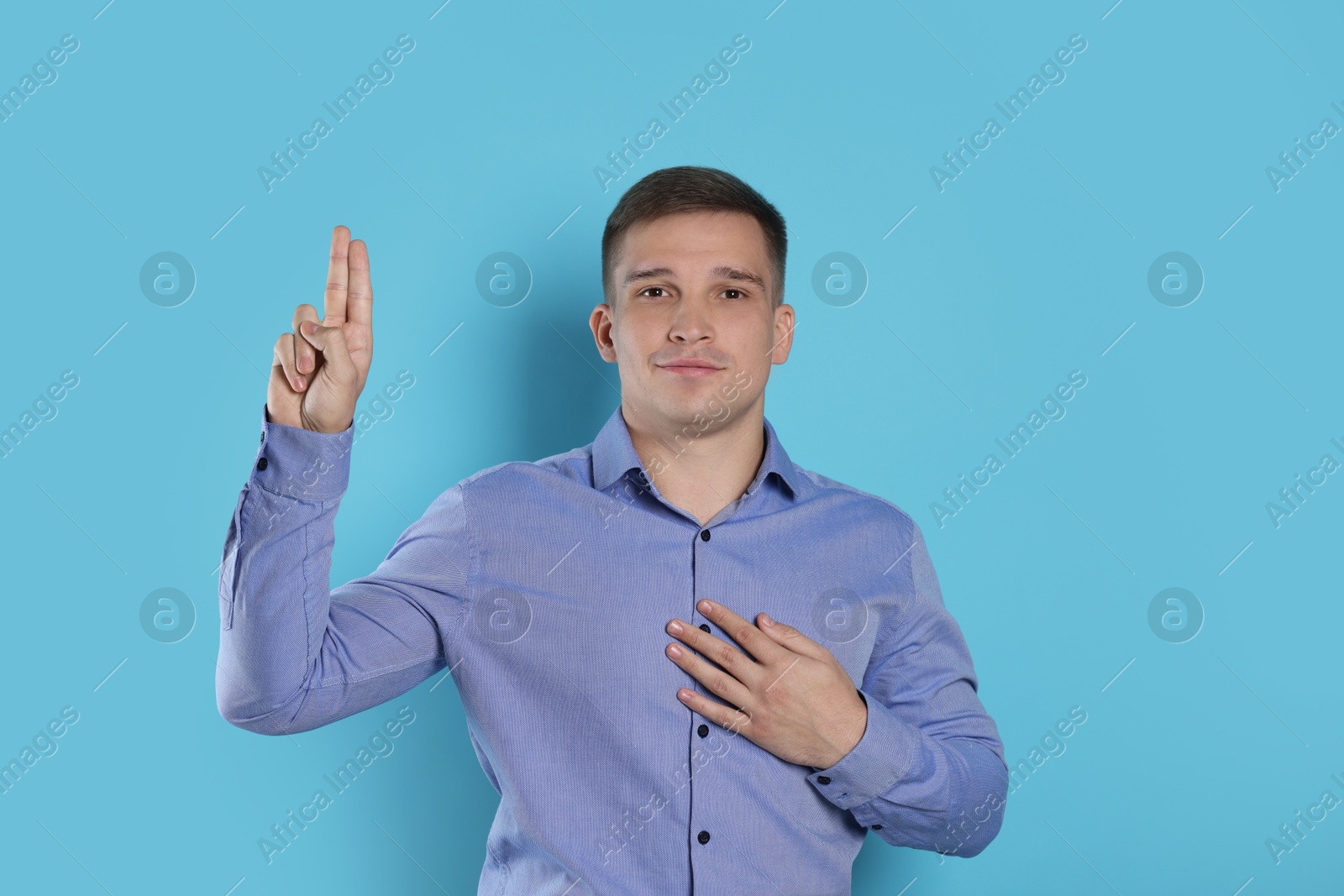 Photo of Man showing oath gesture on light blue background. Making promise