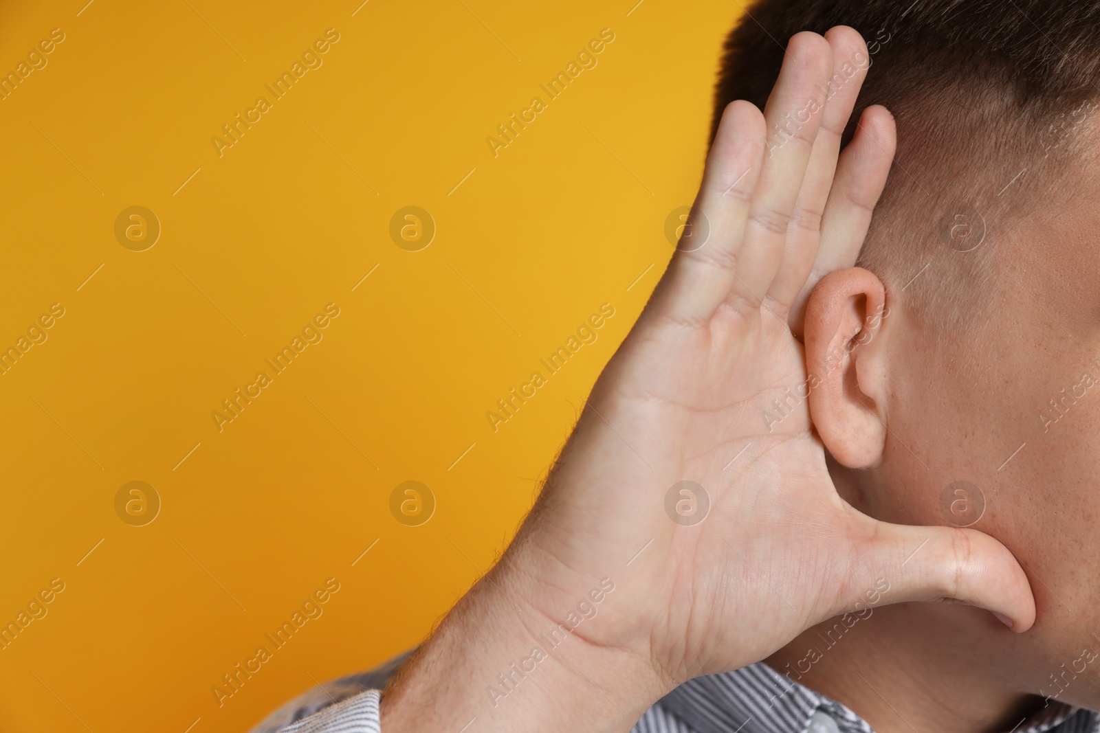 Photo of Man showing hand to ear gesture on orange background, closeup. Space for text