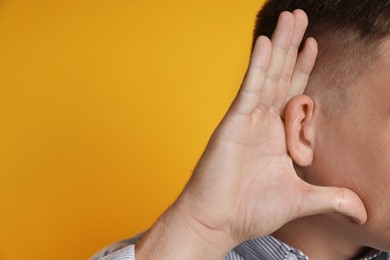 Photo of Man showing hand to ear gesture on orange background, closeup. Space for text